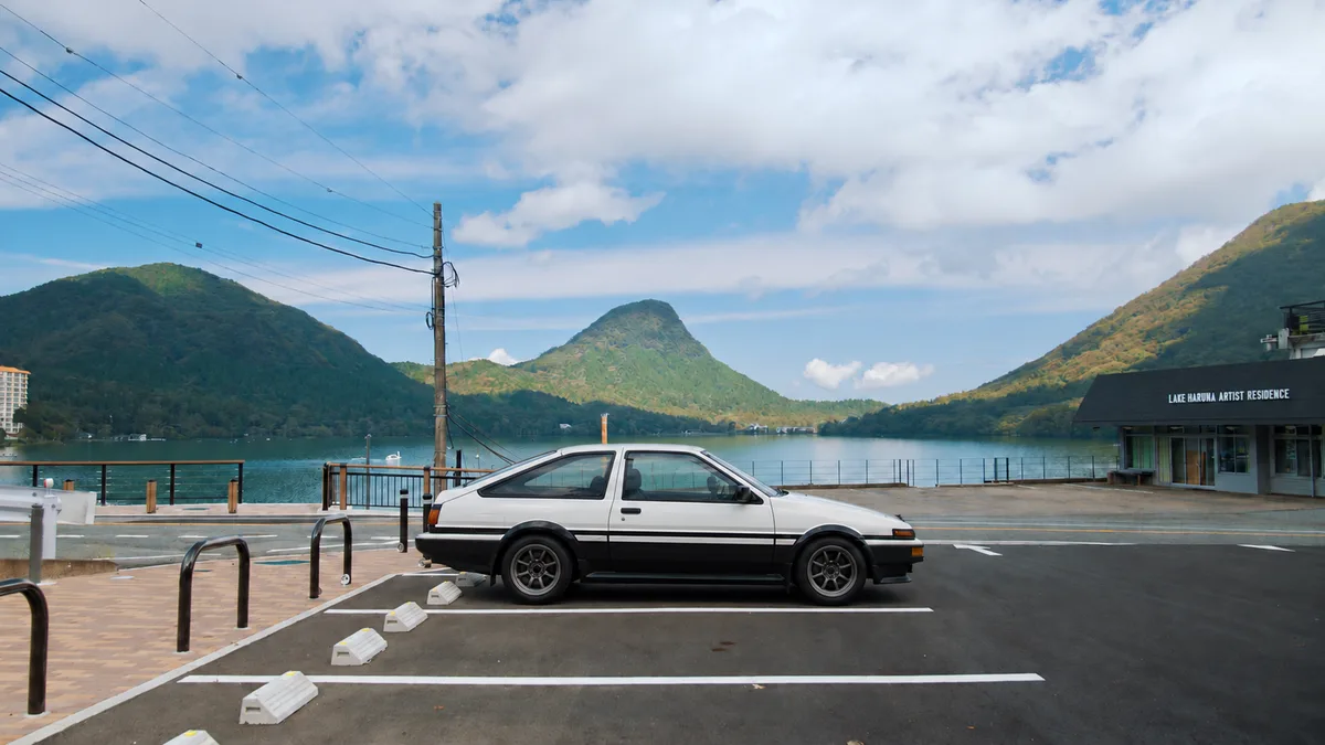 A white AE86 beside Lake Haruna with mountains behind