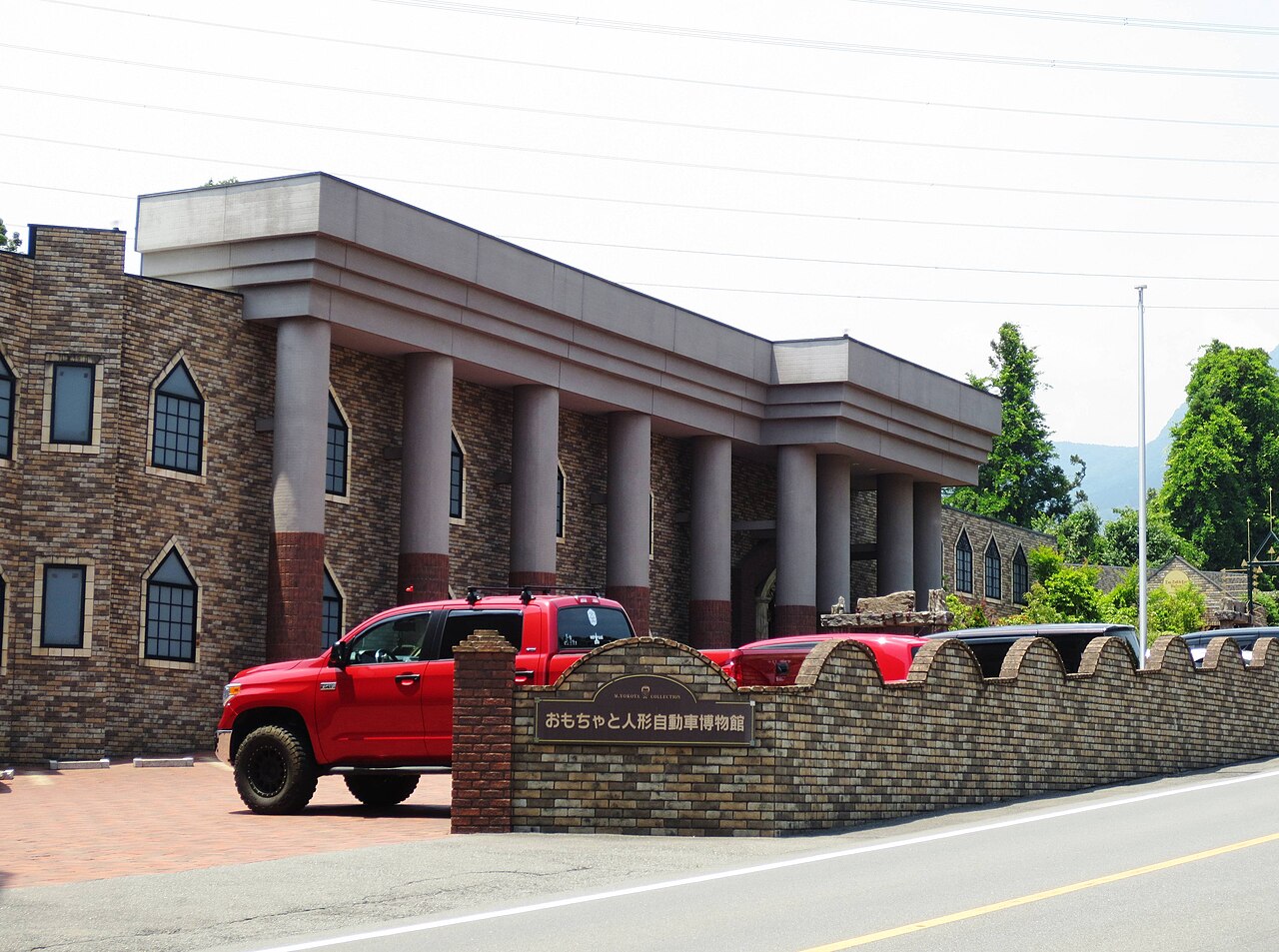 The brick and column front of the Ikaho Toy, Doll and Car Museum with a red pickup in the car park